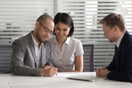 Smiling couple signs a prenup together while their attorney looks on